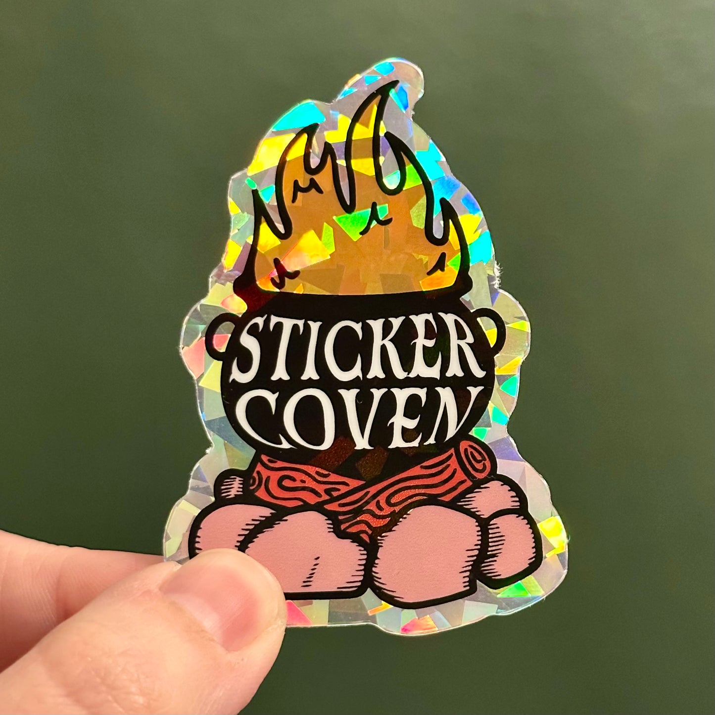 Holographic prism sticker with a cauldron logo and the text "Sticker Coven"