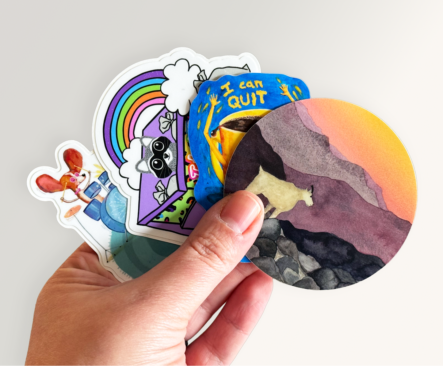Hand holding a collection of colorful stickers with various designs on a light gray background