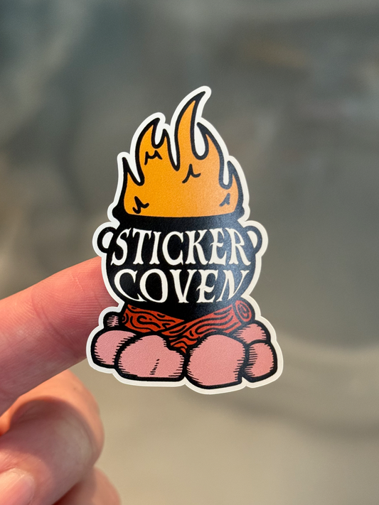 finger holding economy cauldron sticker against grey background 