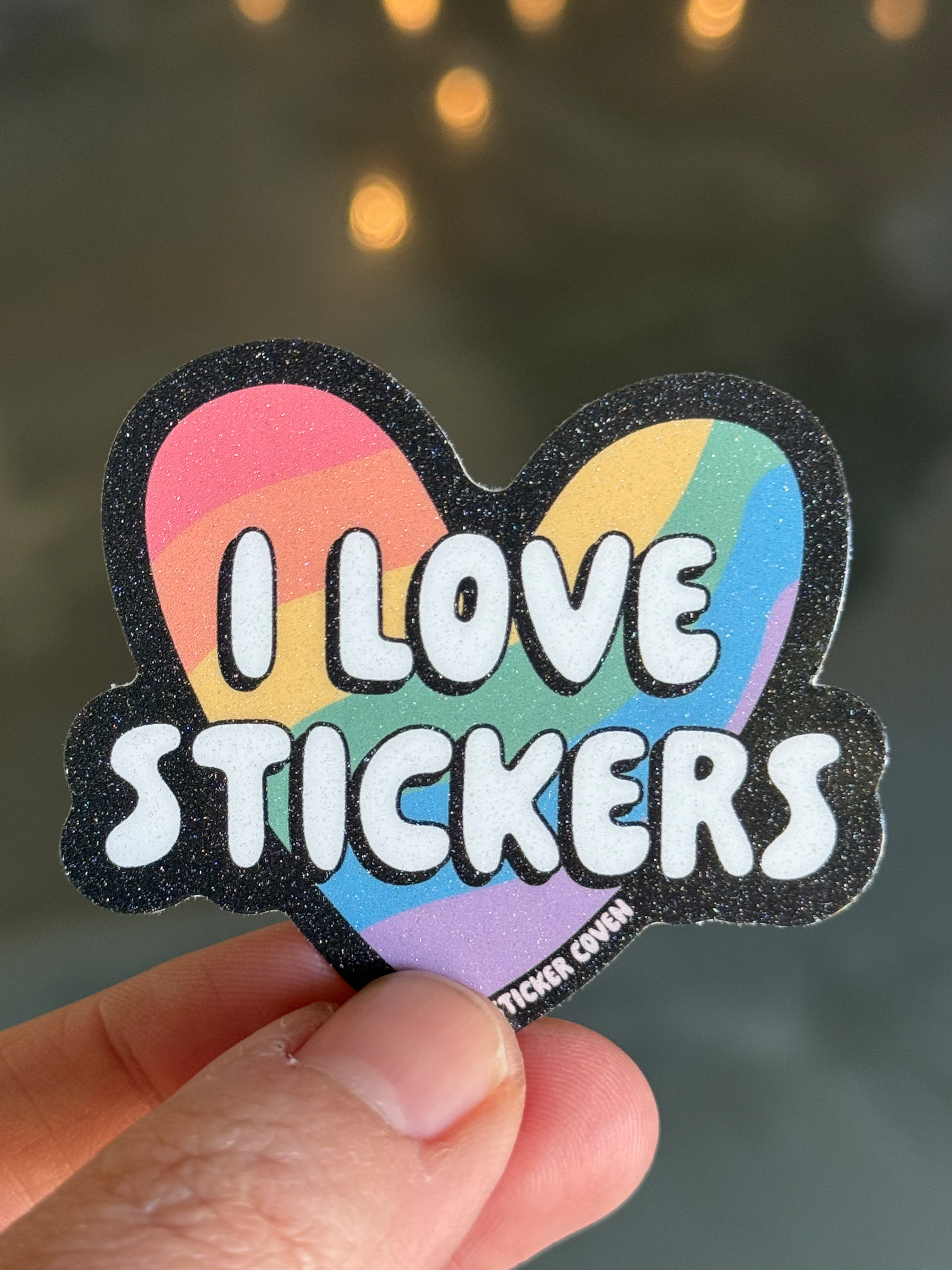 Heart-shaped sticker with 'I Love Stickers' text held by a hand against a blurred background